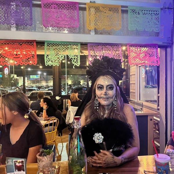 Woman in Day of the Dead makeup and costume at a restaurant with colorful papel picado.