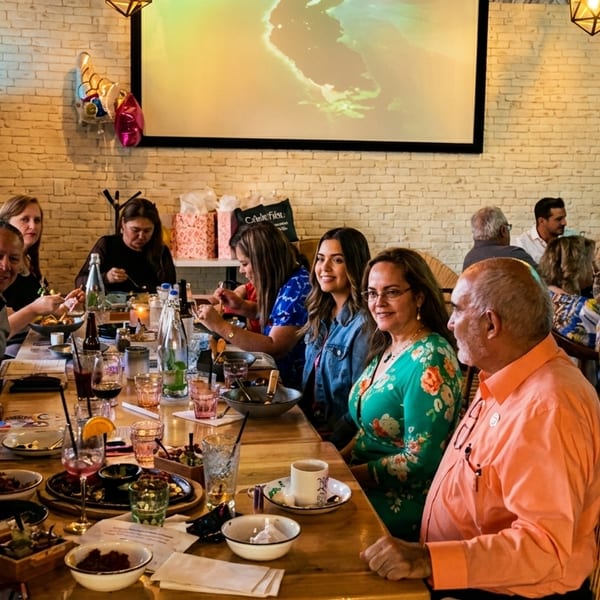 Diverse group of people dining together at a long wooden table in a restaurant with brick walls.