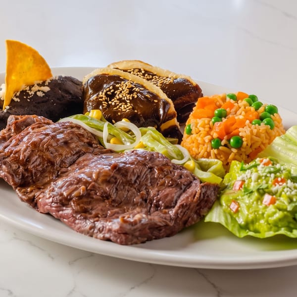 Platter with steak, rice, guacamole, refried beans, and two mole enchiladas on a white marble surface.