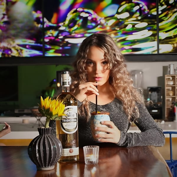 Woman with curly hair sips a drink at a bar next to a bottle of Jose Cuervo tequila.