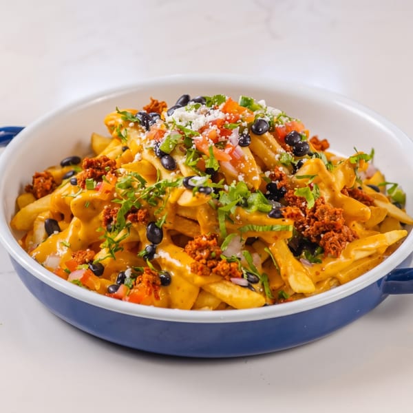 Loaded fries with cheese sauce, black beans, chorizo, pico de gallo, and cilantro in a blue and white dish.